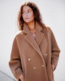 Close up of woman model standing in front of white wall wearing MaxMara Camel Coat