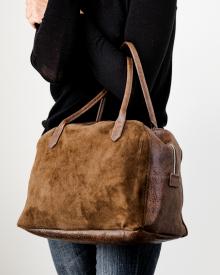 Woman wearing black sweater and blue jeans holding sand B. May bag