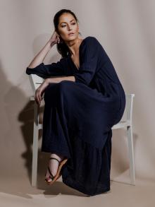 Model wearing navy long dress sitting in chair